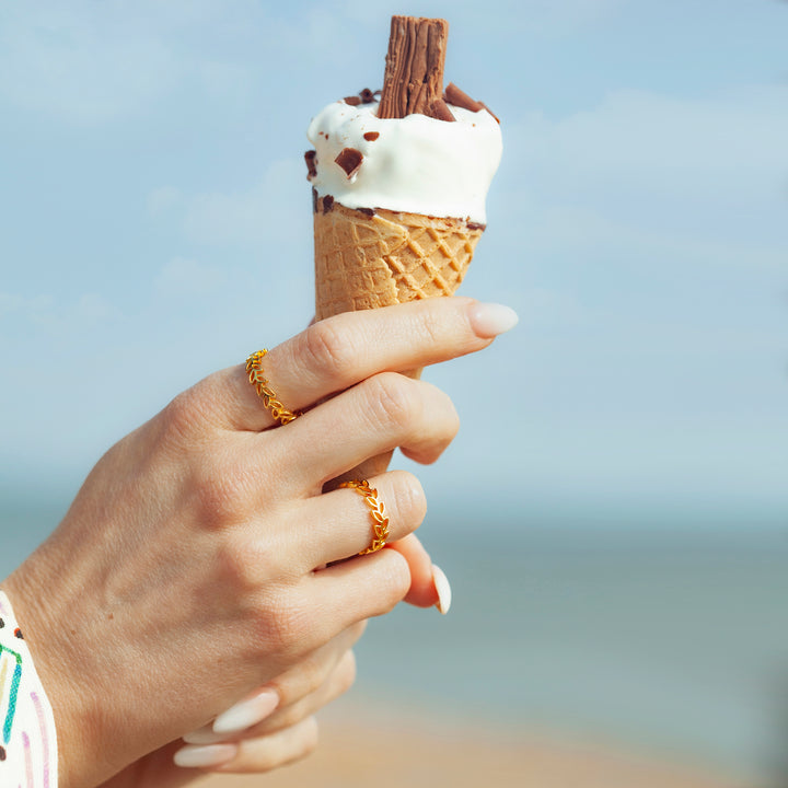Hand with ice cream and two gold garland design rings at beach