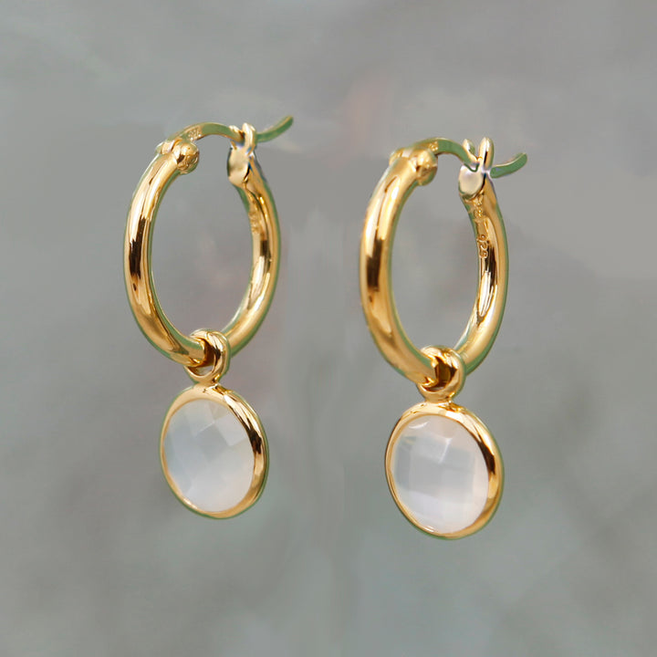 Moonstone hoop earrings in gold on a gray background.