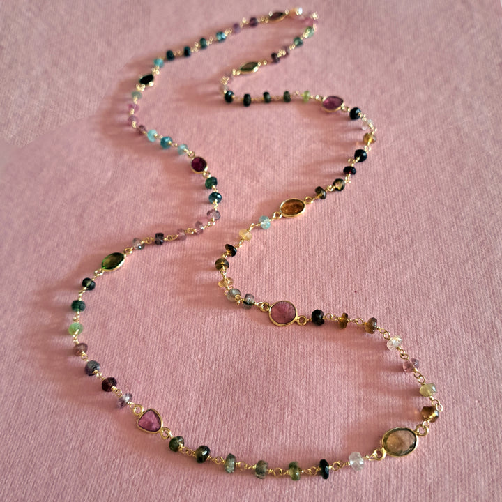 Multicolored tourmaline beaded  necklace in gold on a pink background.