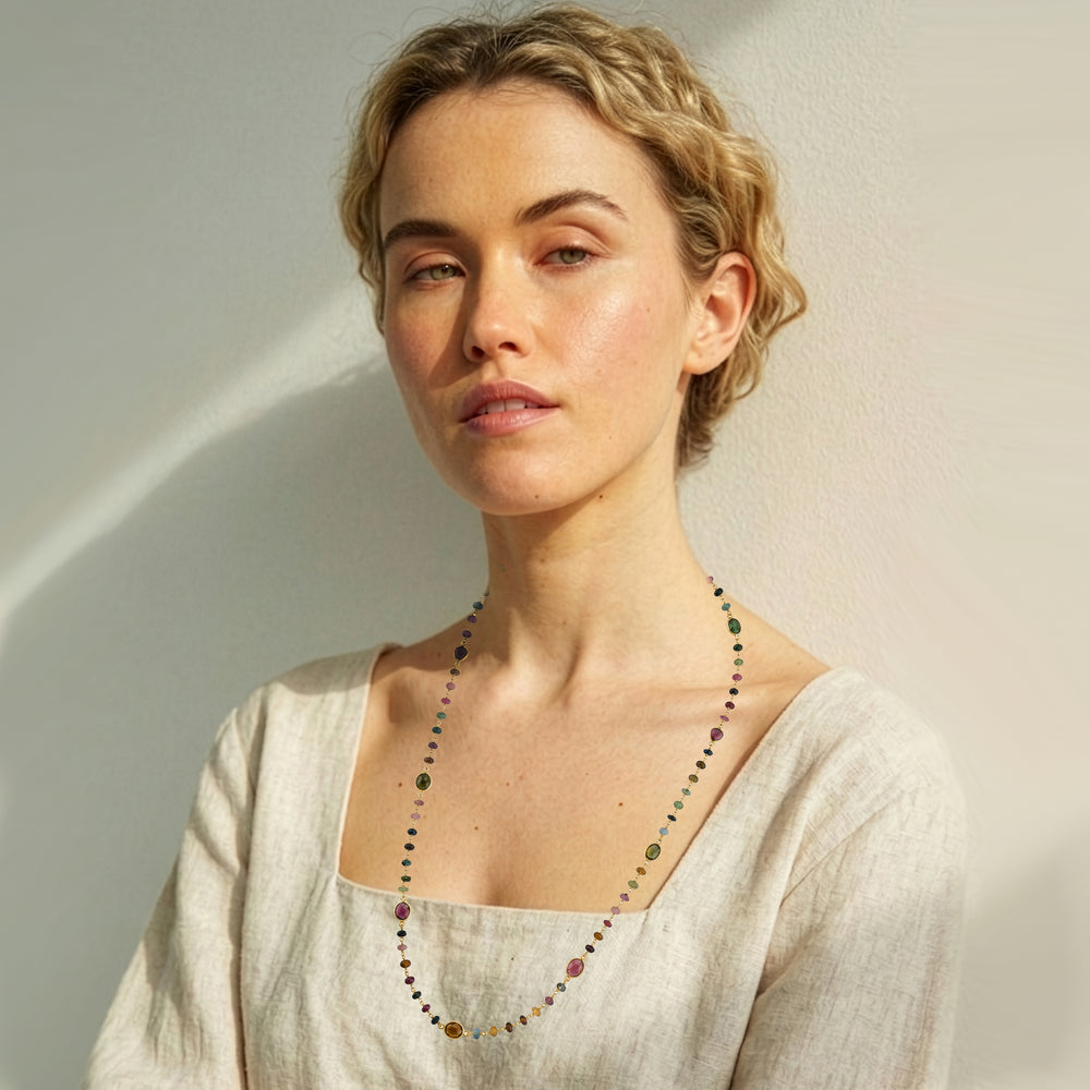 Woman wearing a long tourmaline strand necklace in gold on a beige background.