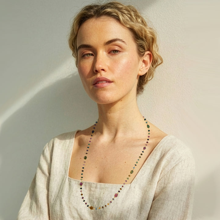 Woman wearing a long tourmaline strand necklace in gold on a beige background.