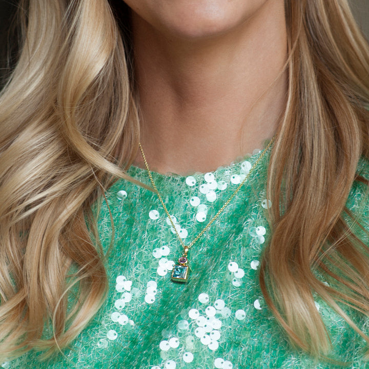 Close-up of a person wearing a green sequined top and a gold necklace blue topaz and amethyst gemstones