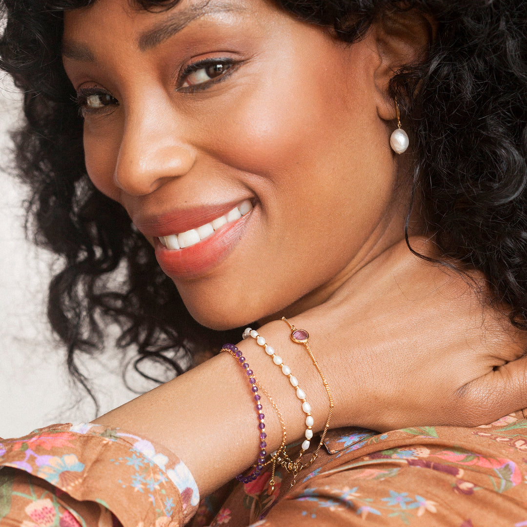 Woman wearing three gold bracelets with pearl and moonstone beads.