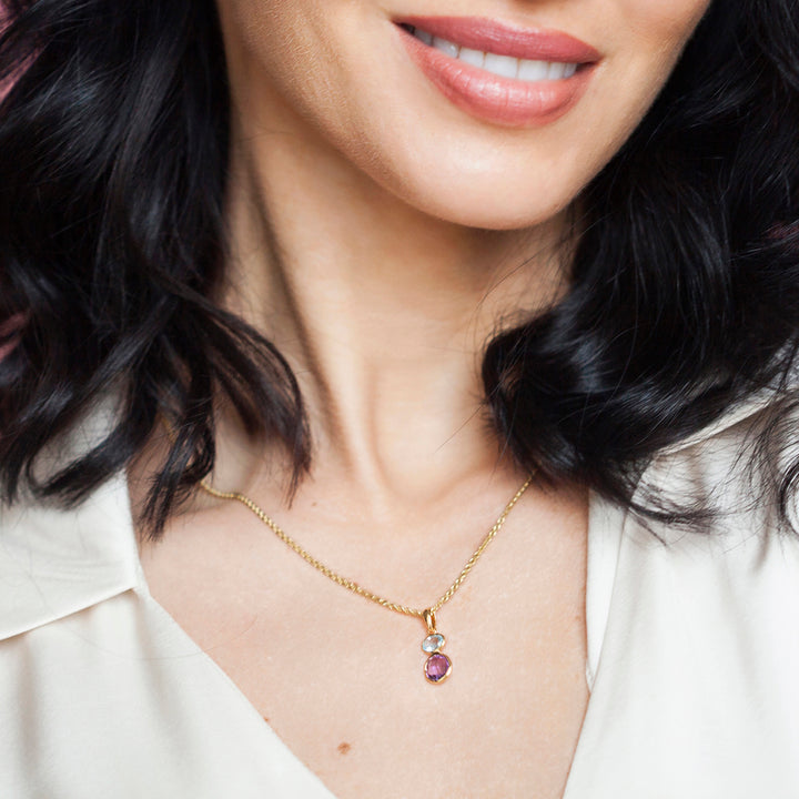 Close-up of a woman wearing a gold necklace with purple and blue gemstones