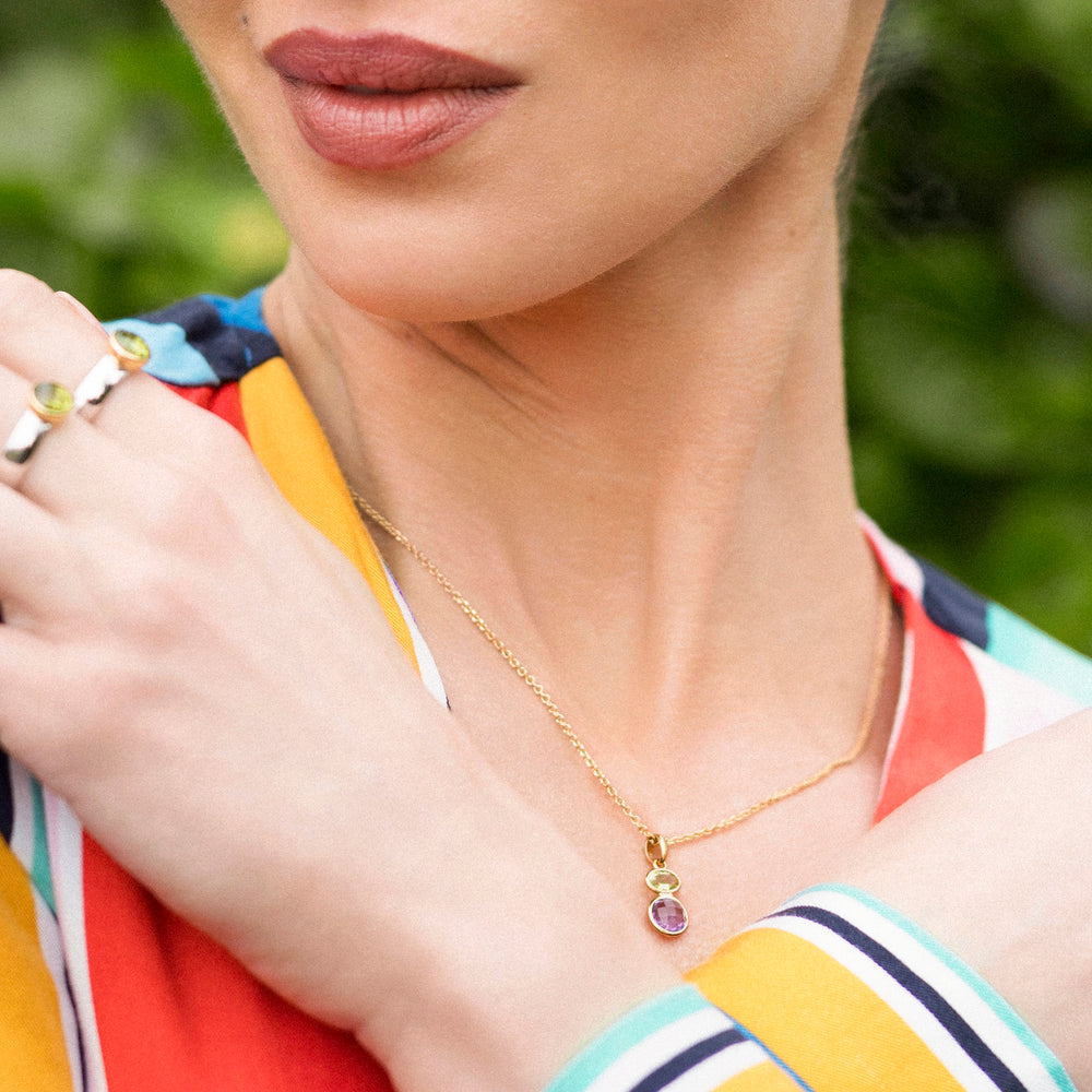 Close-up of a person wearing a gold necklace and pendant set with purple and green gemstones