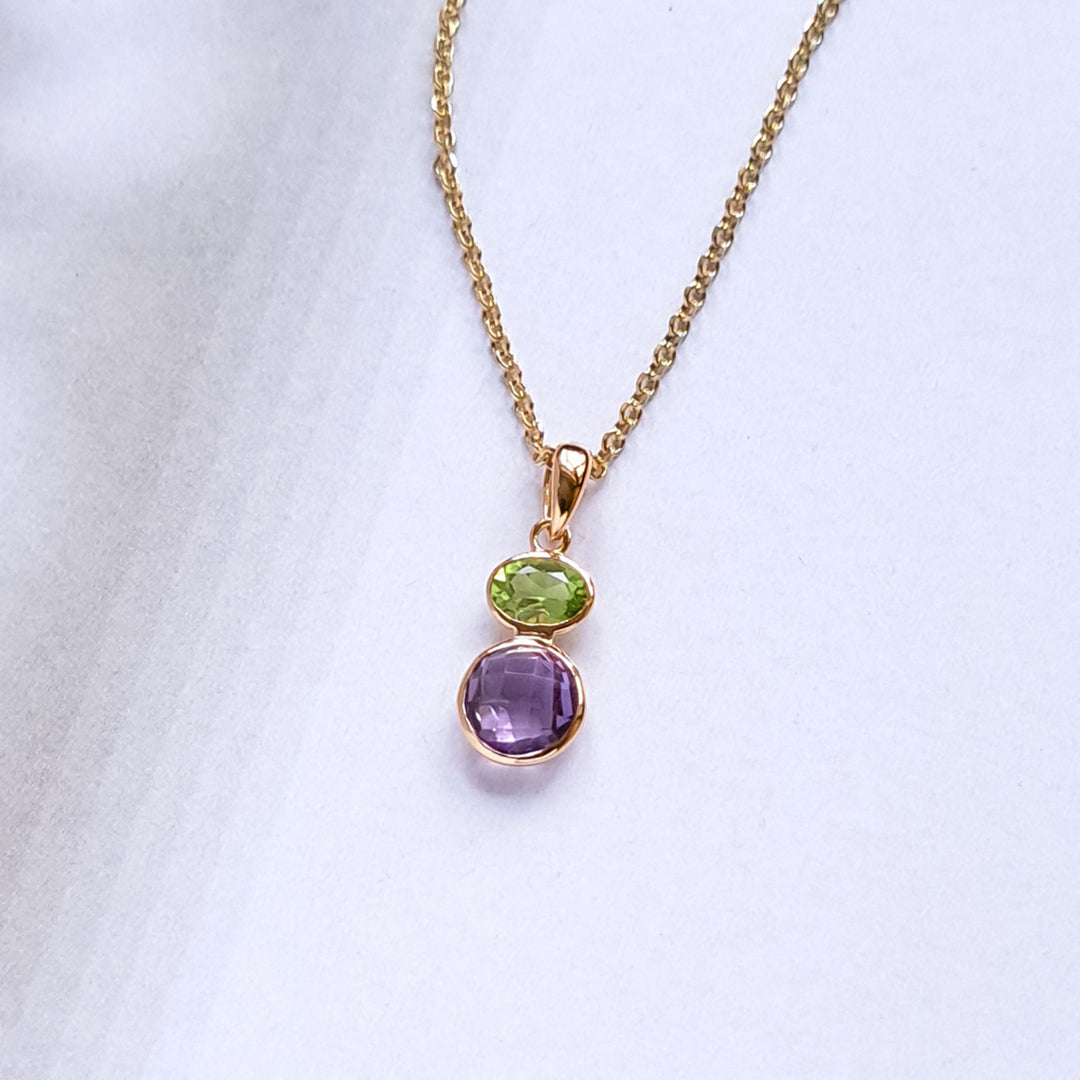 Gold necklace with a pendant featuring purple and green gemstones on a white background