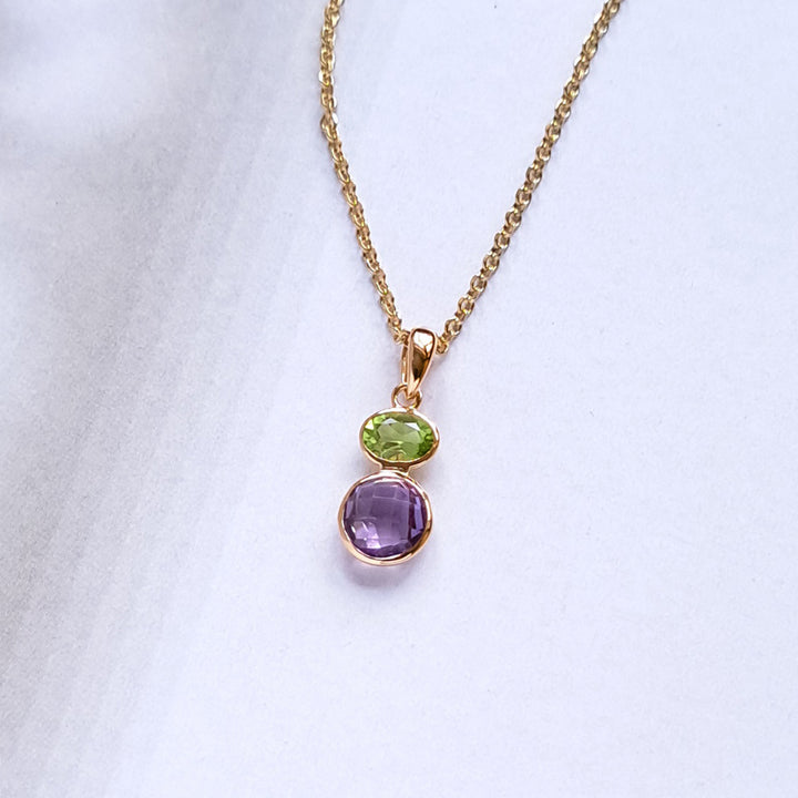 Gold necklace with a pendant featuring purple and green gemstones on a white background