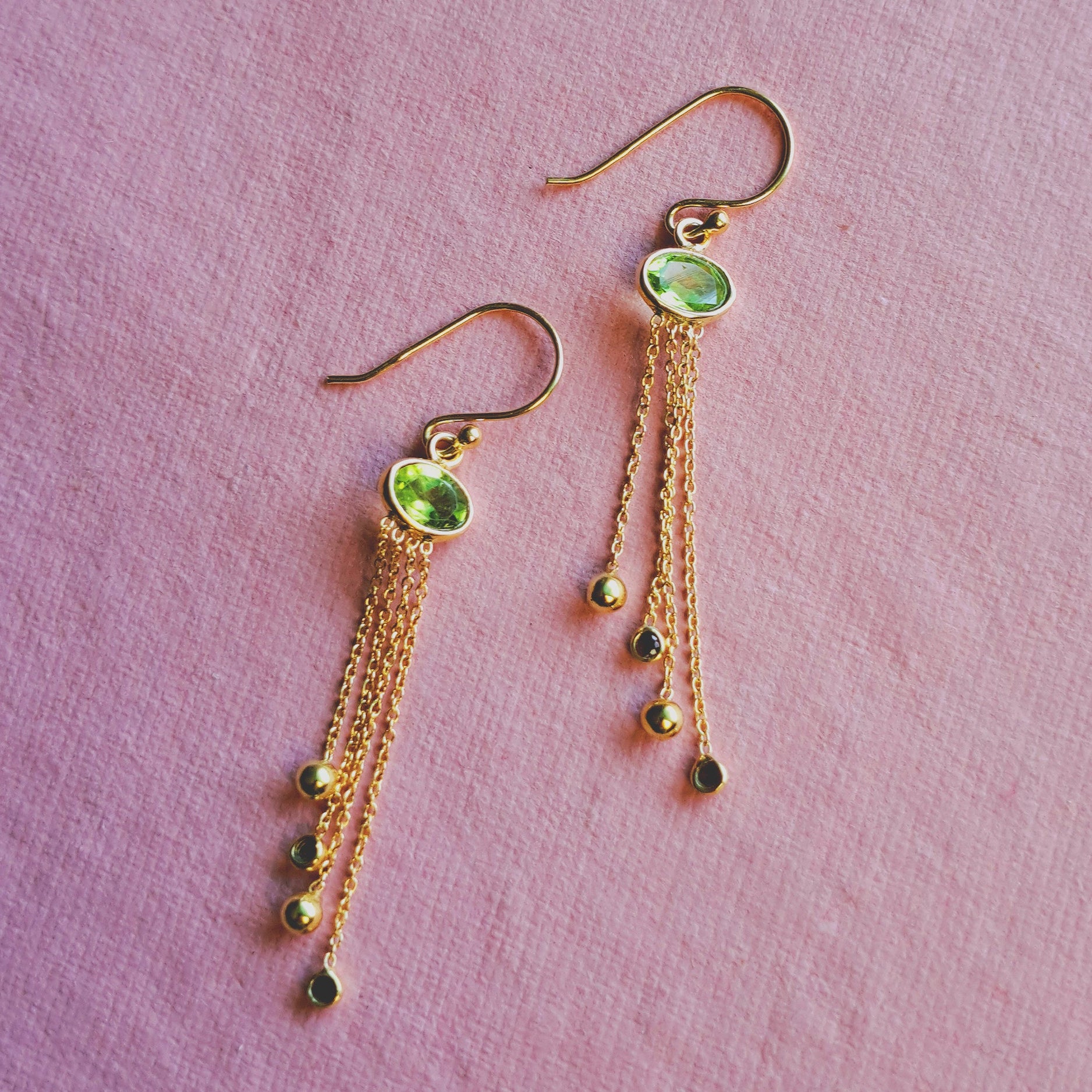 18ct gold vermeil peridot chandelier drop earrings with garnets against a pink background