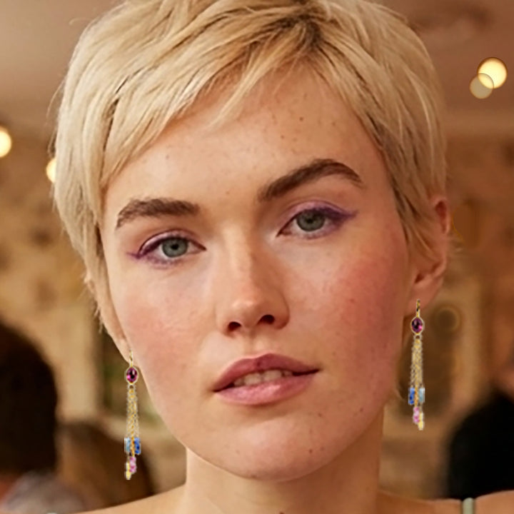 Close-up of woman wearing delicate gold drop earrings with pink tourmalines with beaded sapphire drops.