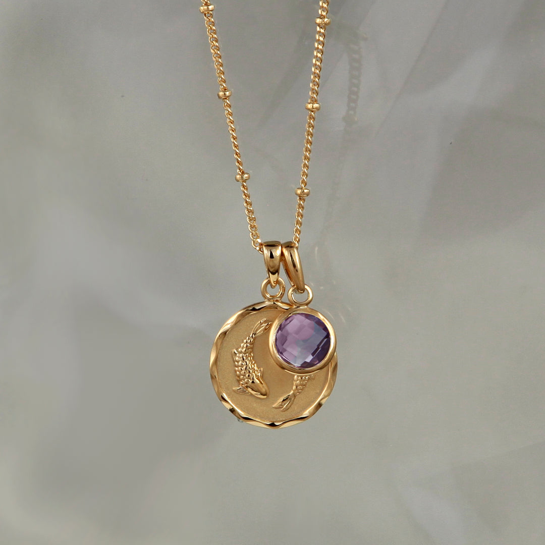 Gold zodiac necklace with pisces star sign and amethyst february charm on gray background