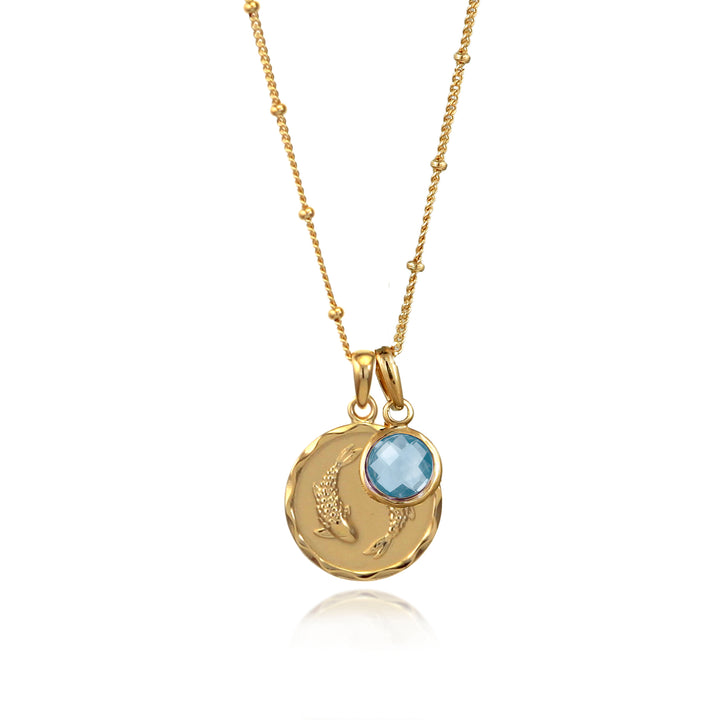 Gold zodiac necklace with pisces star sign and blue topaz birthstone charm on white background