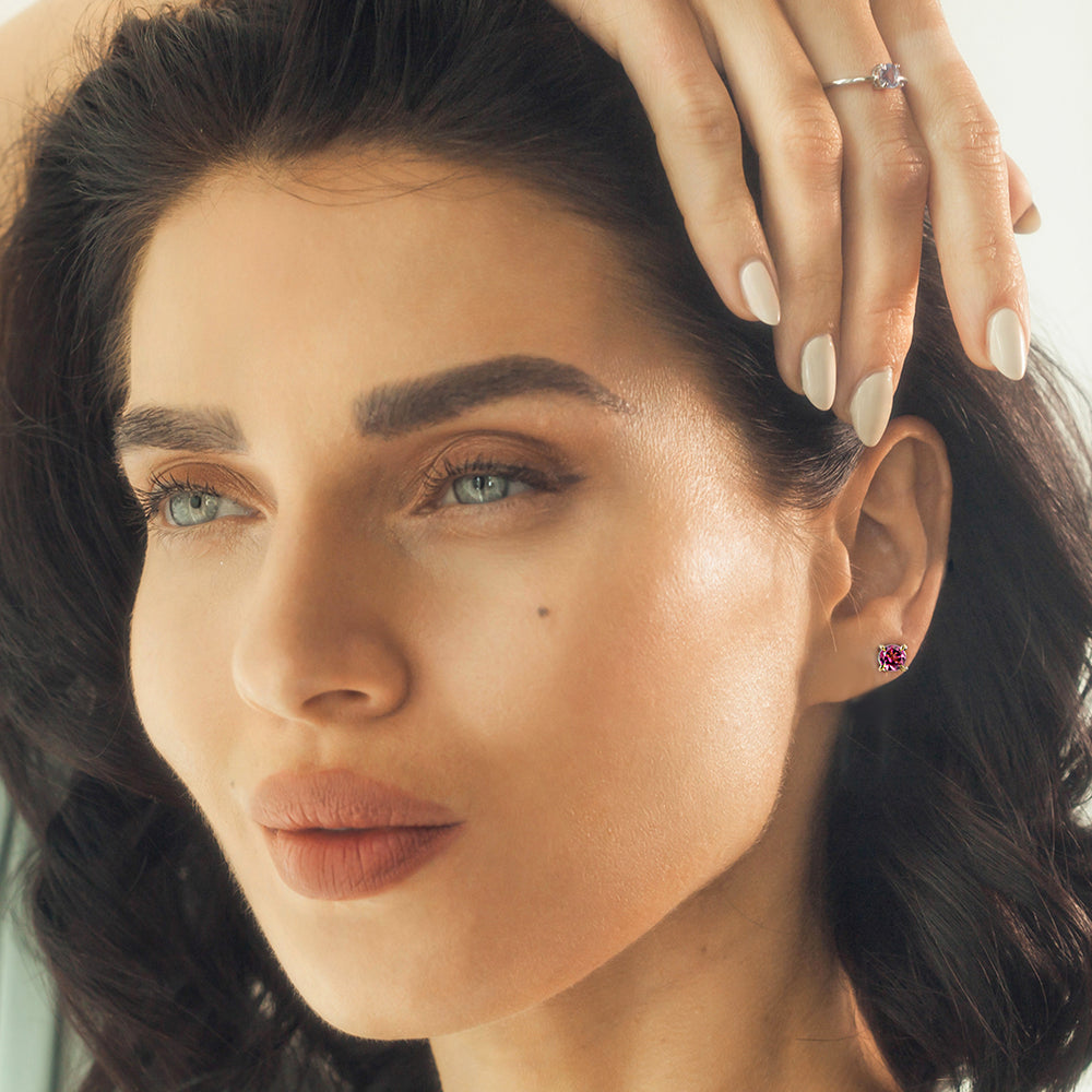 Close-up of a woman wearing gold stud earrings set with pink gemstones