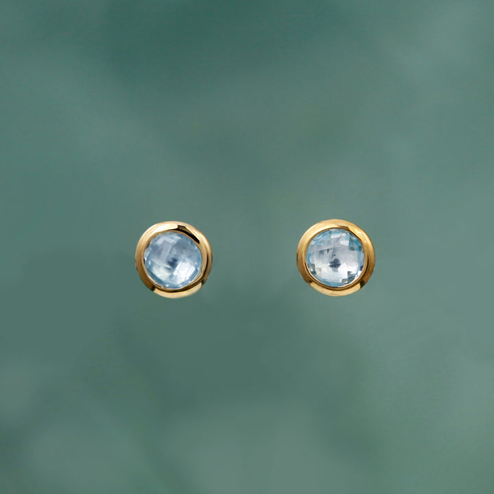 Gold stud earrings with genuine blue topaz gemstones on an aqua background