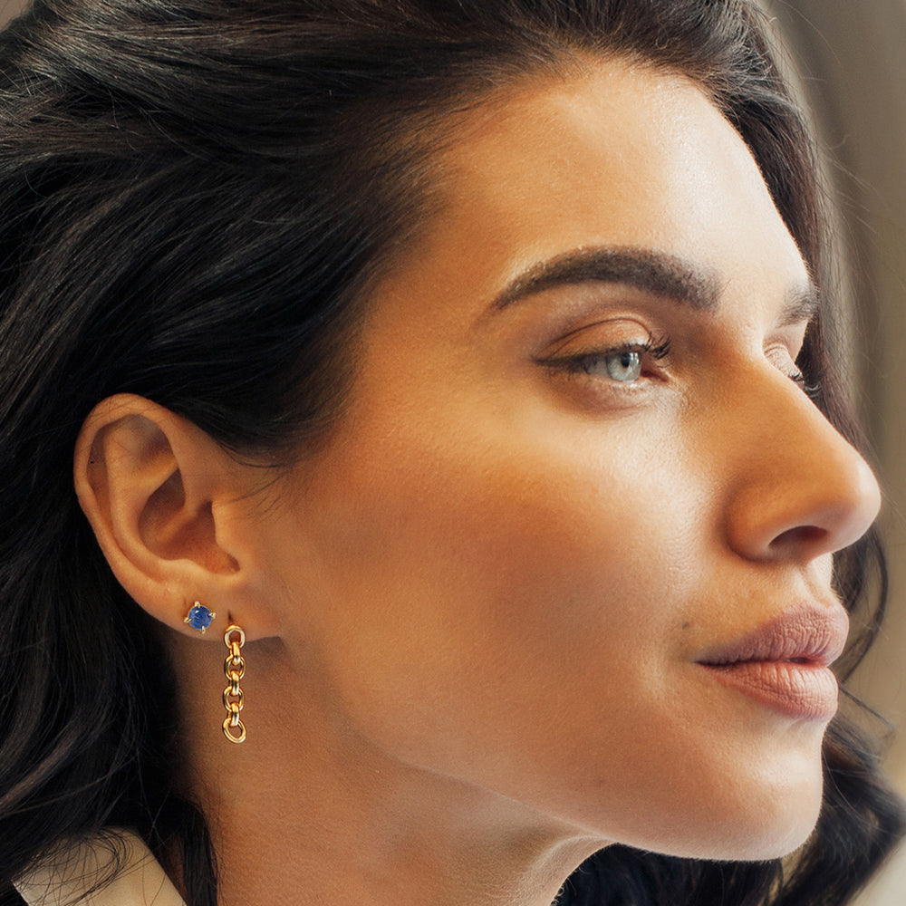 Close-up of a woman wearing a gold stud earring with a blue sapphire gemstone.