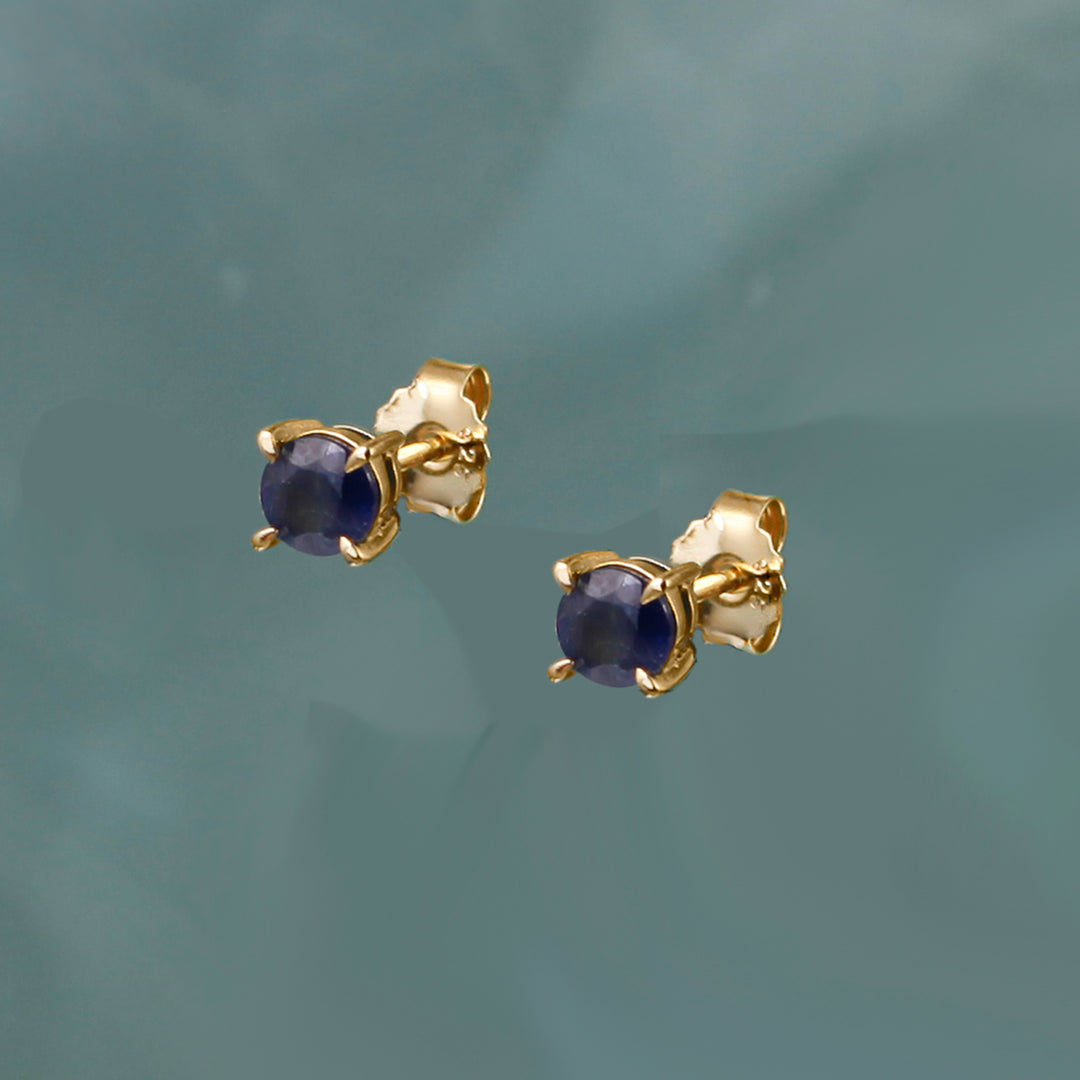 Gold earrings with deep blue sapphire  gemstones on a gray background