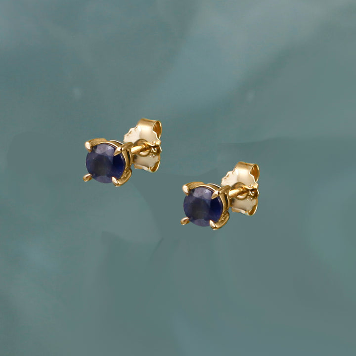 Gold earrings with deep blue sapphire  gemstones on a gray background