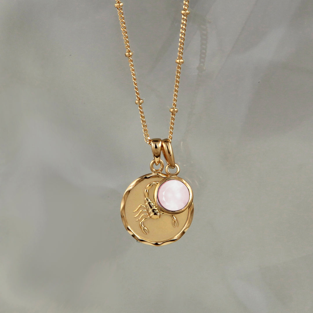 Gold zodiac necklace with scorpio star sign and rose quartz october charm on gray background