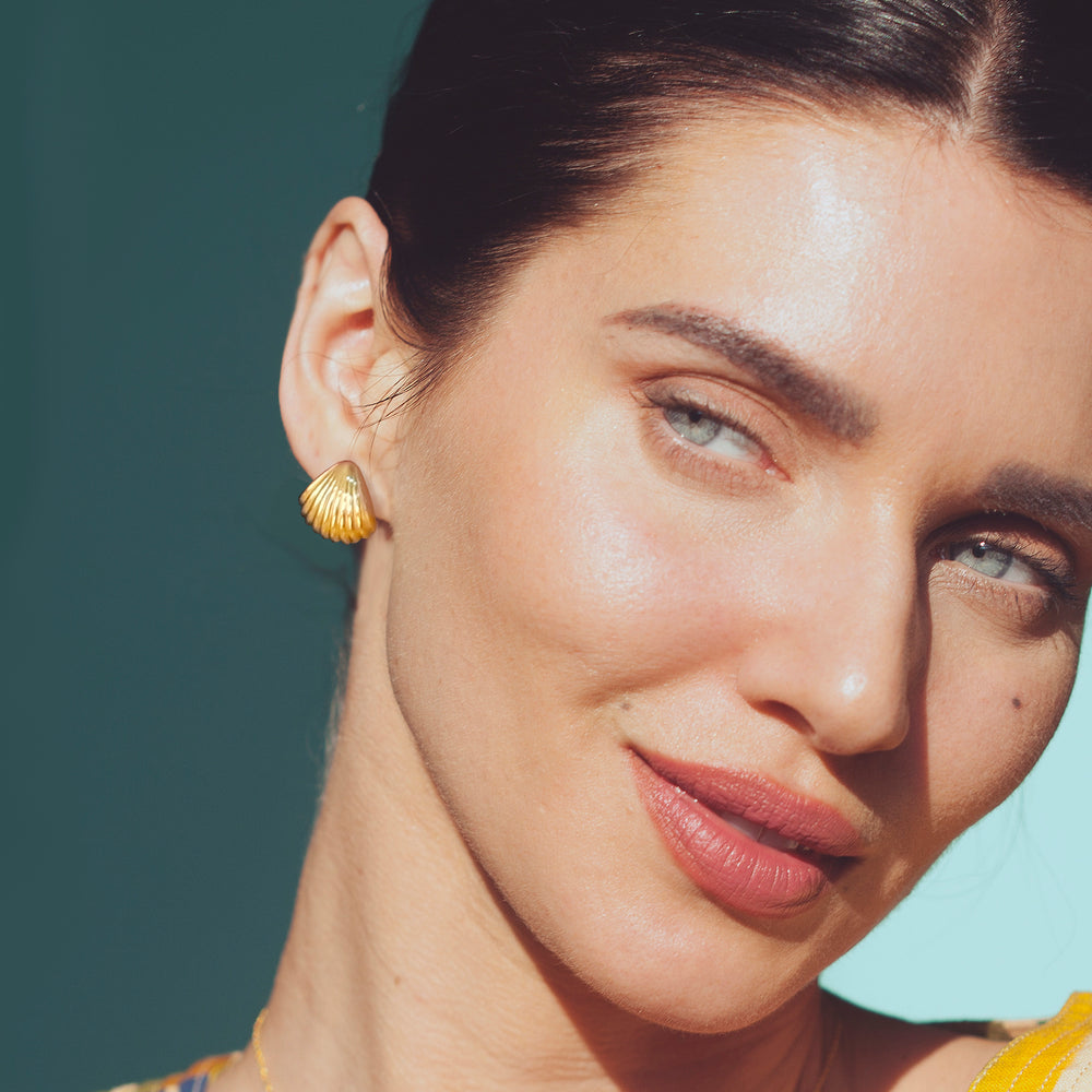 Close-up of a woman wearing gold seashell earrings with a blue background