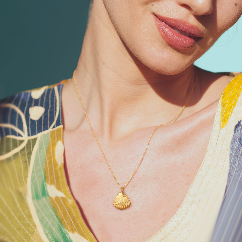 Woman wearing a gold necklace with a clamshell pendant against a neutral background