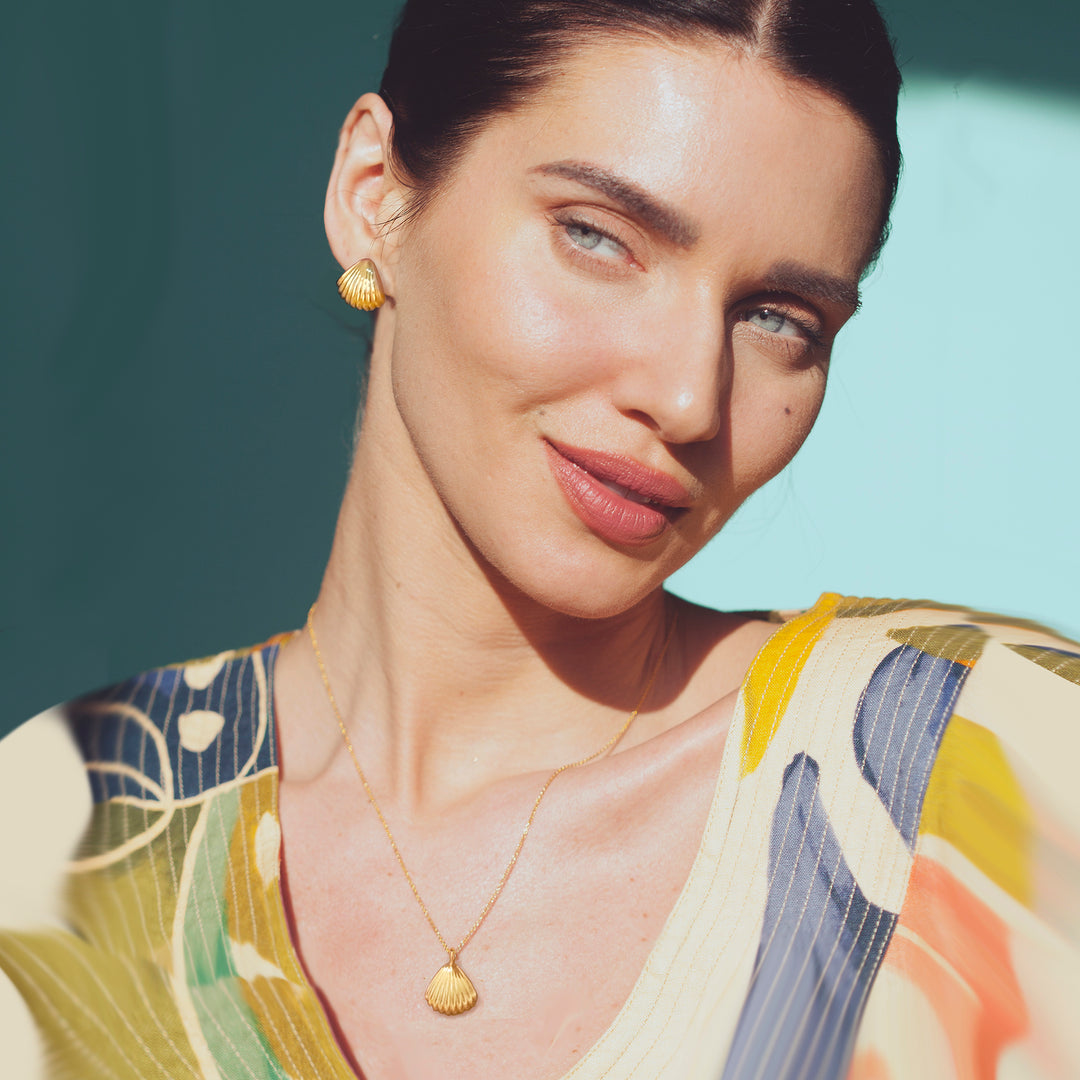 Woman wearing a colorful top with a gold seashell necklace and matching earrings