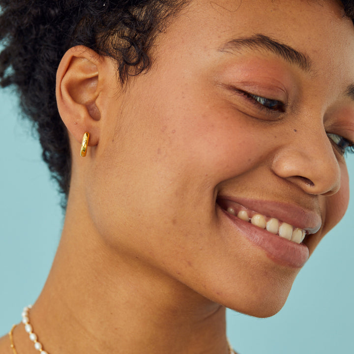 Close-up of a woman wearing a gold earring with a blue background