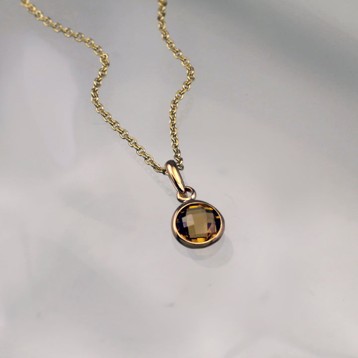 gold pendant necklace with a smoky quartz gemstone on a gray background