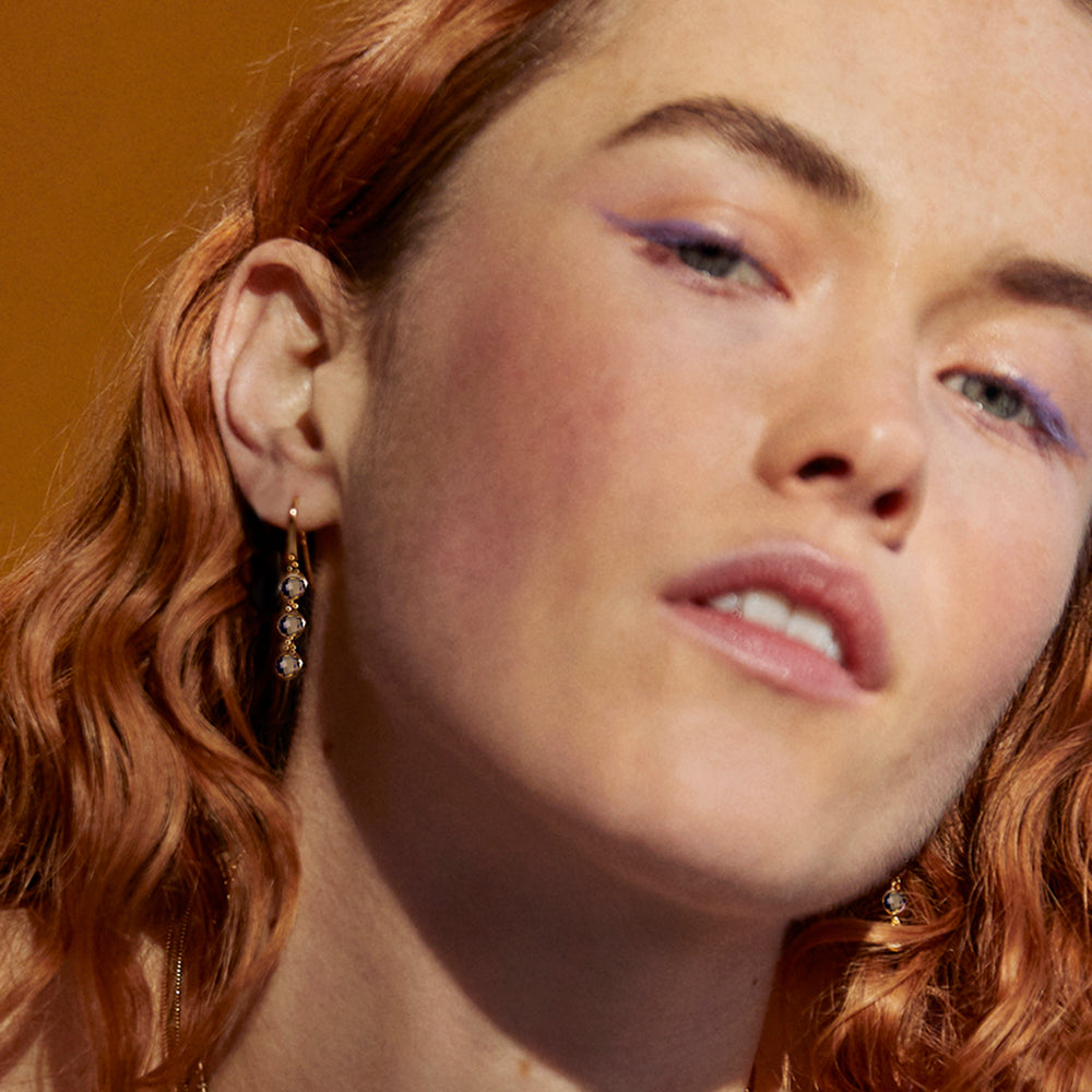 Model wearing gold three stone earrings set with brown gemstones