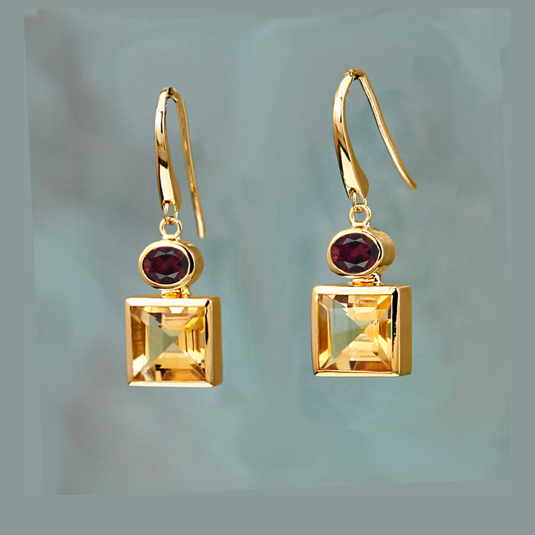 Gold earrings with square citrine gemstones and oval garnet red stones on a gray background