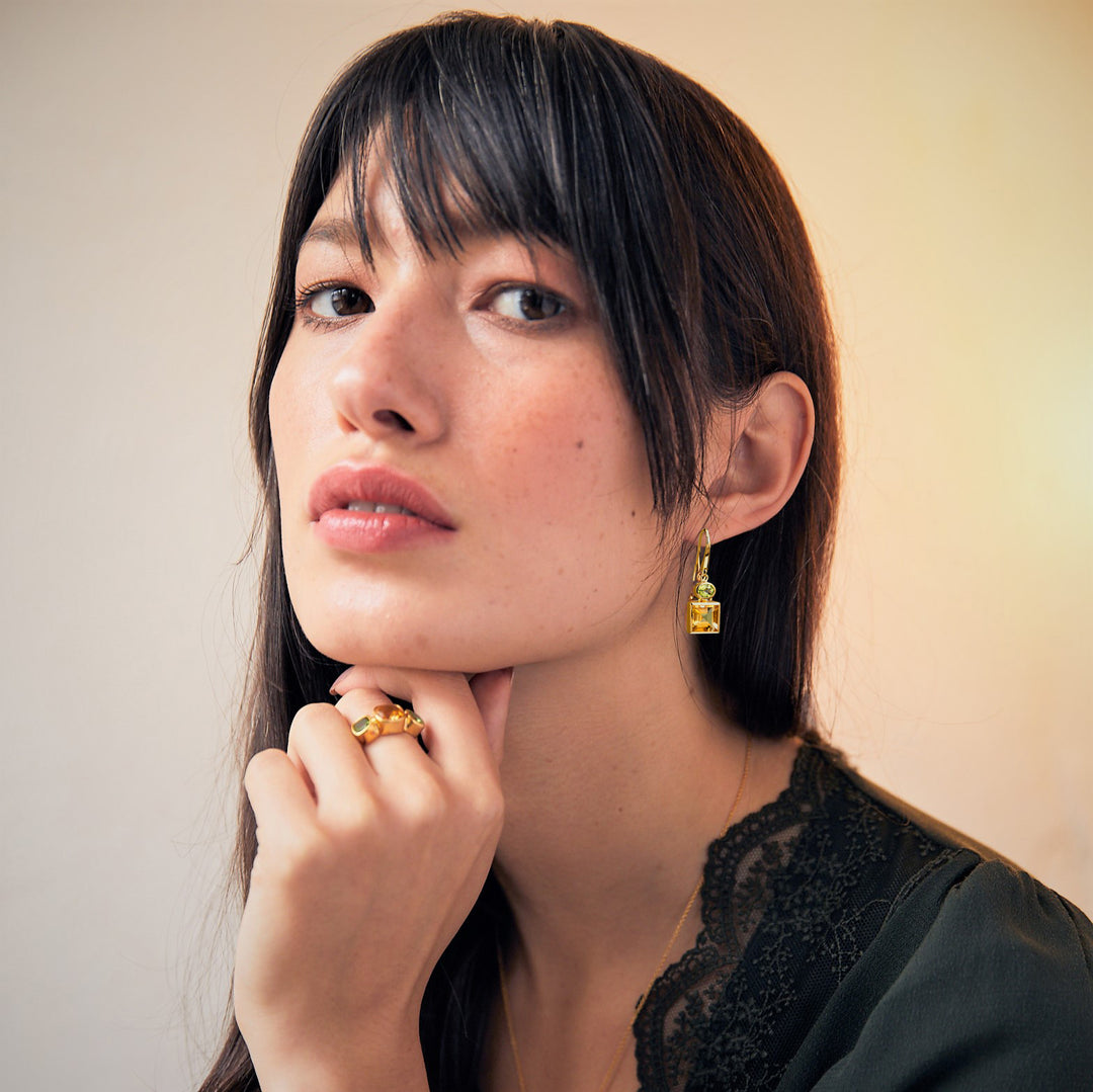 Woman wearing gold gemstone earrings and matching ring with citrine and green peridot gems.
