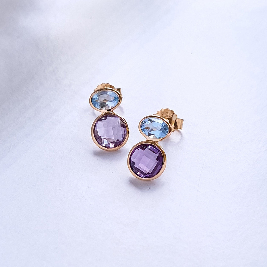 Pair of gold earrings with purple and blue gemstones on a light gray background