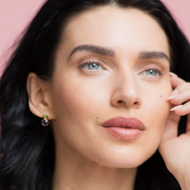 Close-up of a woman wearing an amethyst and peridot earring with a pink background