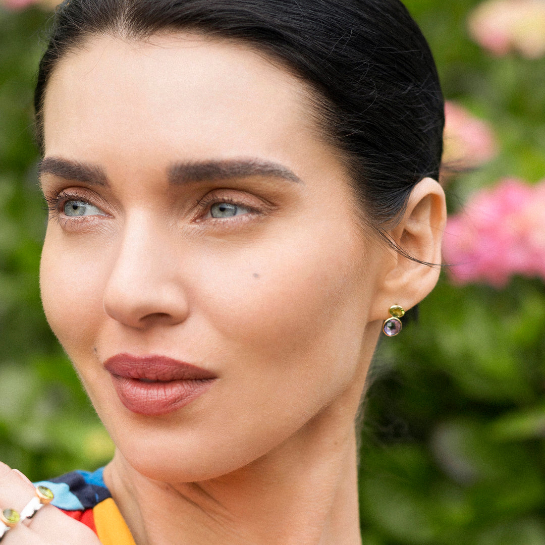 Close-up of a woman with gold and gemstone earrings against a floral background