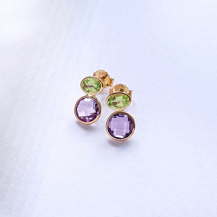 Gold earrings with amethyst and peridot gemstones on a light gray background