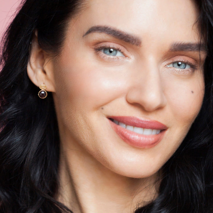 Close-up of a woman wearing gold gemstone post earrings with a dark stone.