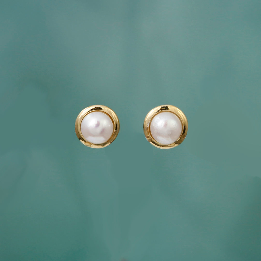 Gold pearl stud earrings on an aqua background