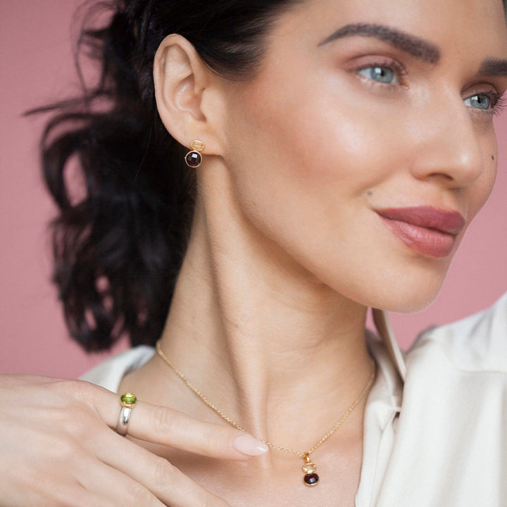 Woman wearing gold gemstone necklace and stud earring set with a pink background