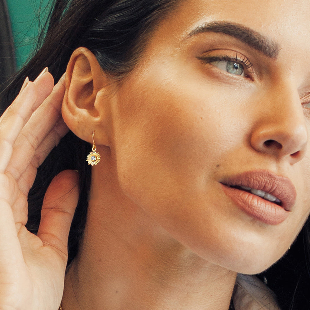 Close-up of model wearing gold sun drop earrings with white topaz