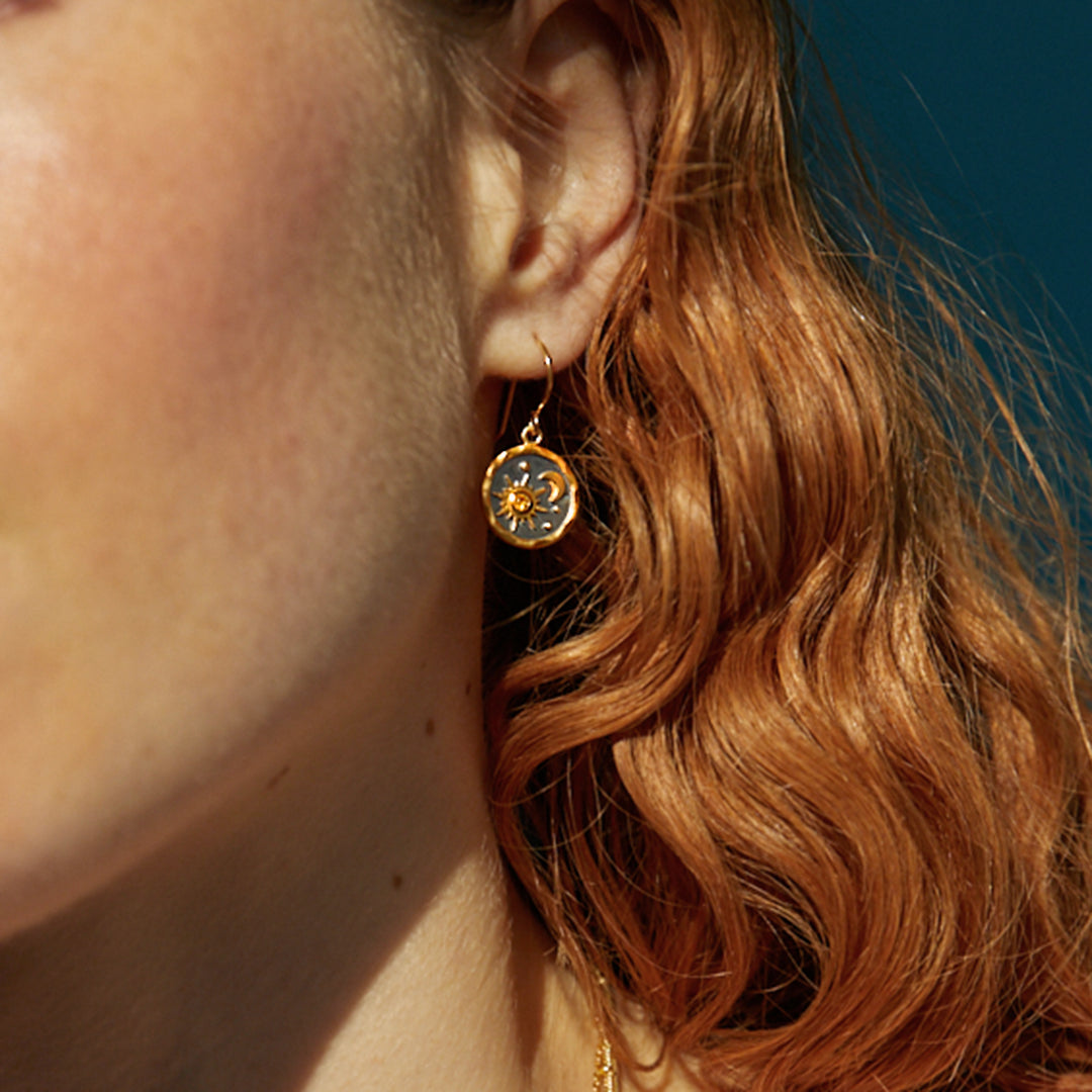 Close-up of model wearing gold sun and moon themed earrings