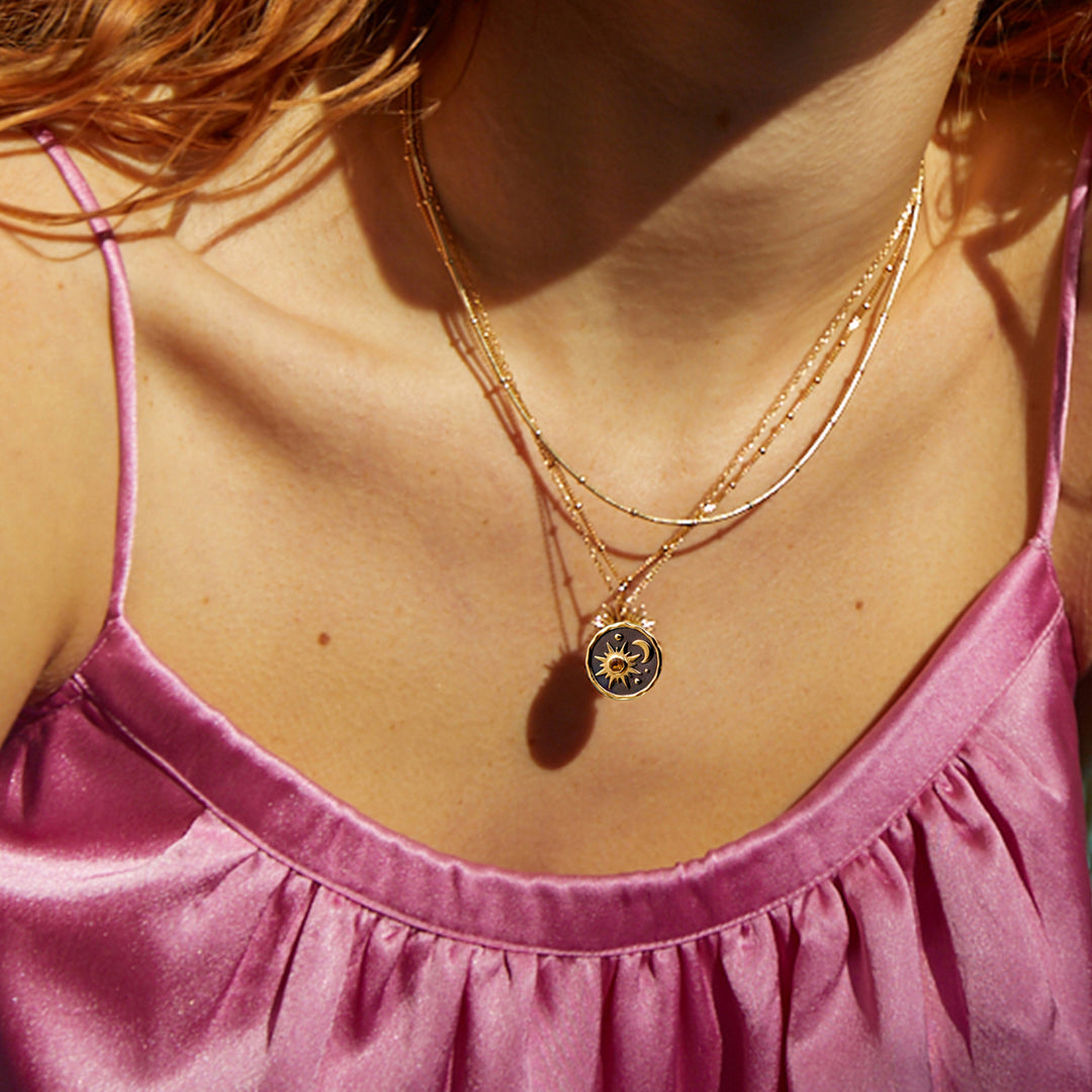 Close-up of model wearing a gold sun and moon themed pendant with chains.
