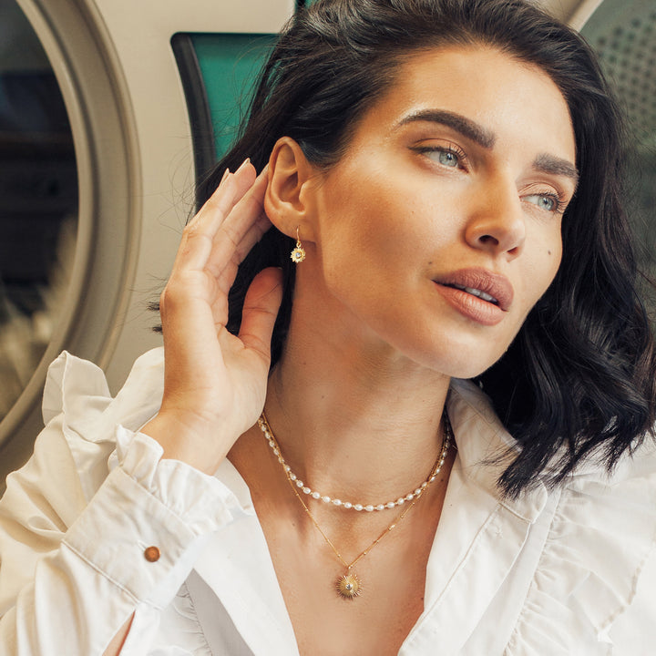Model wearing a gold sun jewellery set with earrings and necklace featuring white topaz gemstone