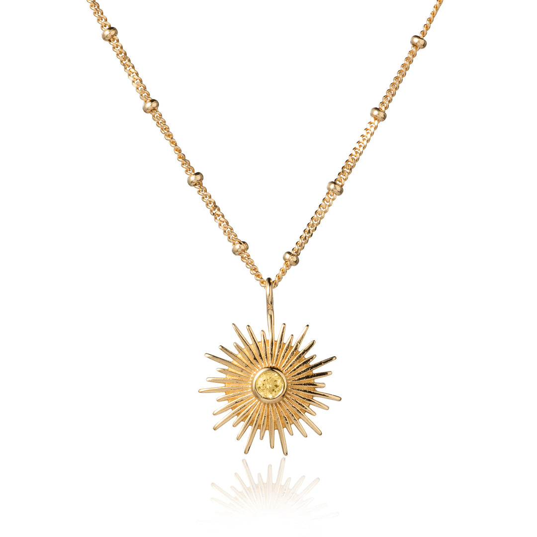 Gold sun necklace on a beaded curb chain with a citrine gemstone on a white background