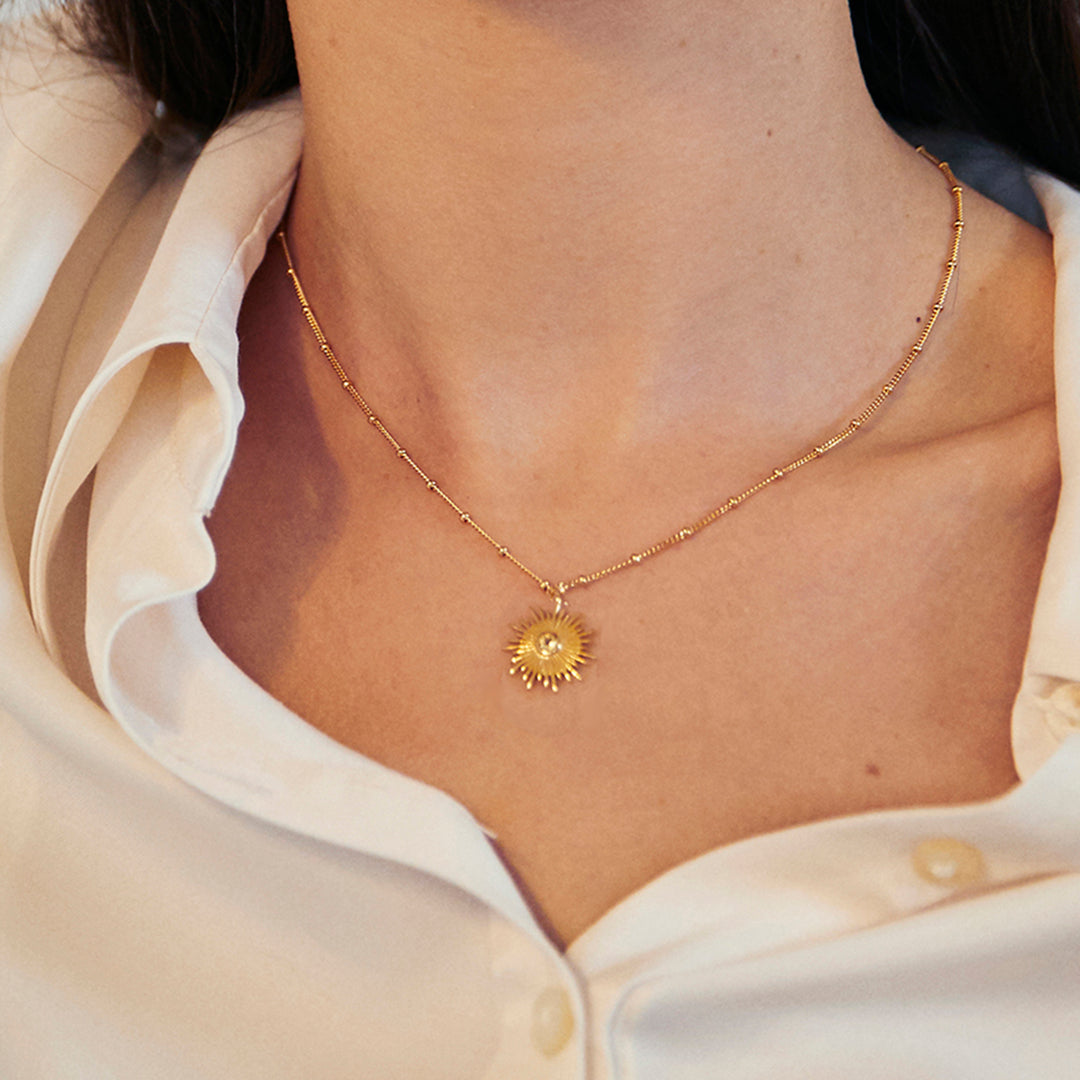 Close-up of model wearing a gold sun necklace with beaded chain set with yellow citrine