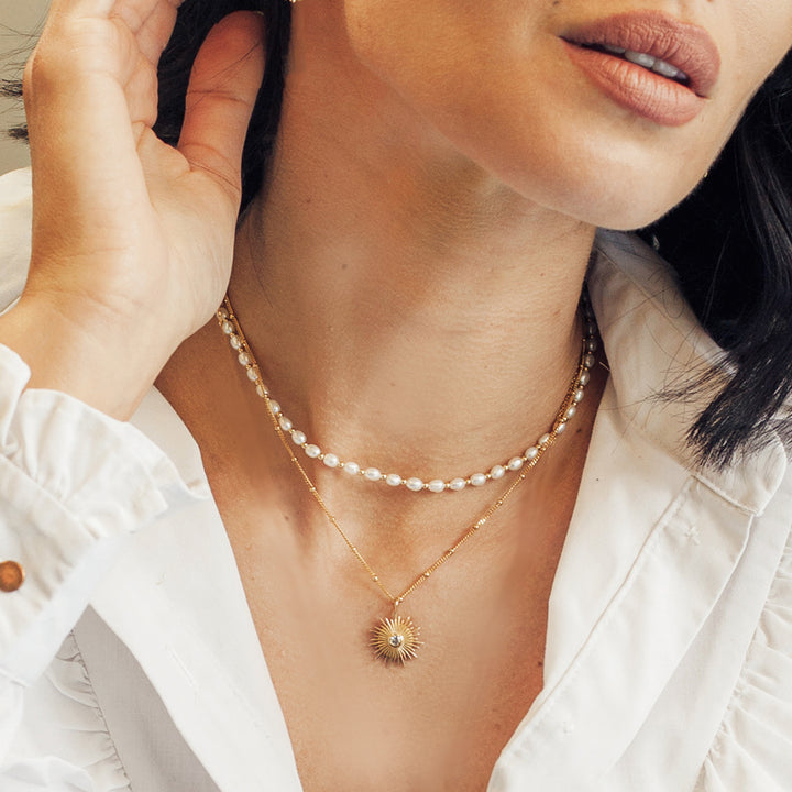 Close-up of model wearing a gold sun necklace set with white topaz and a gold and pearl choker.