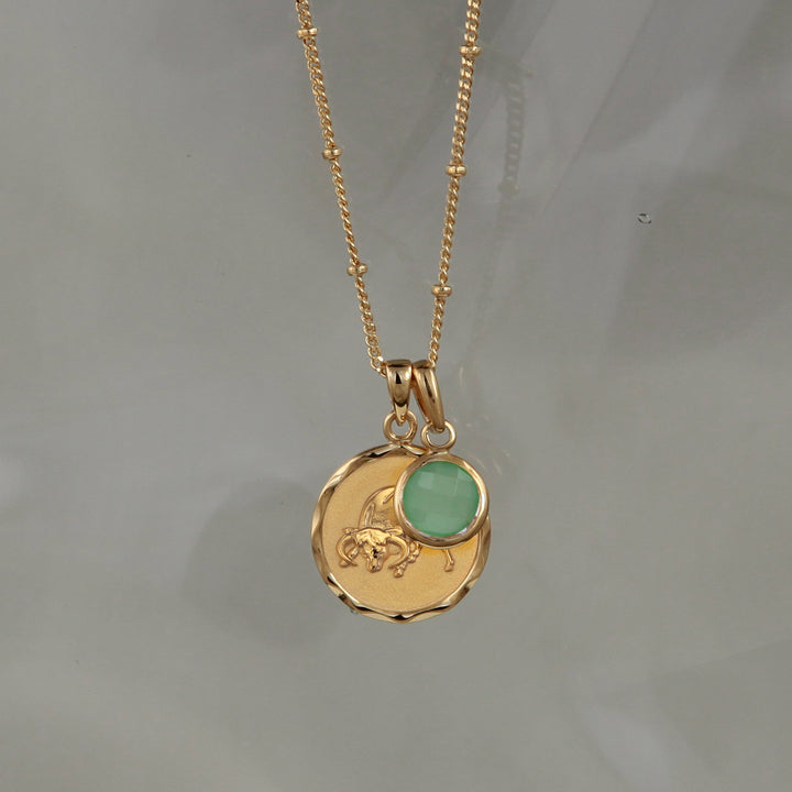 Gold Taurus star sign pendant necklace with a Green Quartz May birthstone charm on a gray background