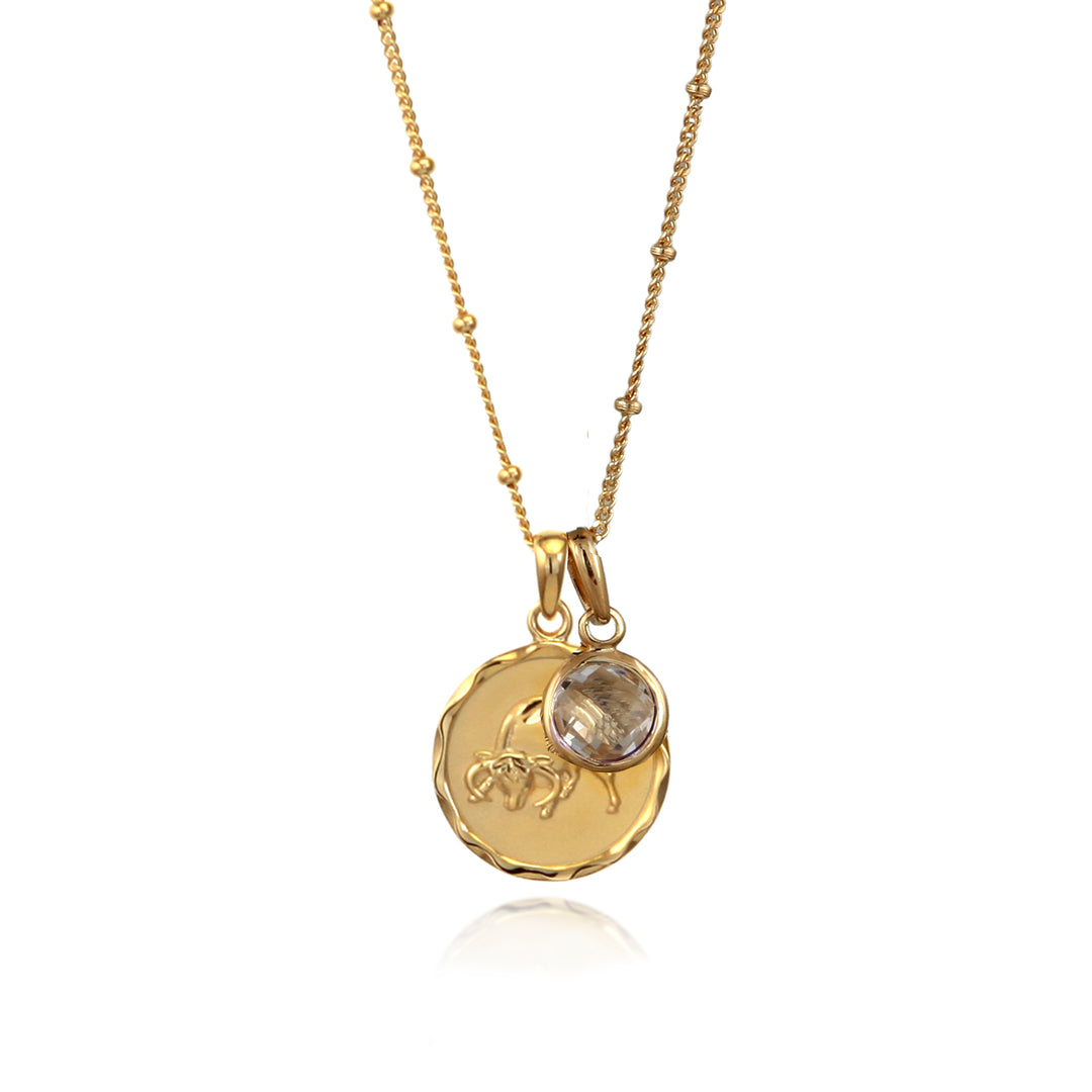 Gold Taurus zodiac pendant necklace with a white topaz April birthstone charm on a white background