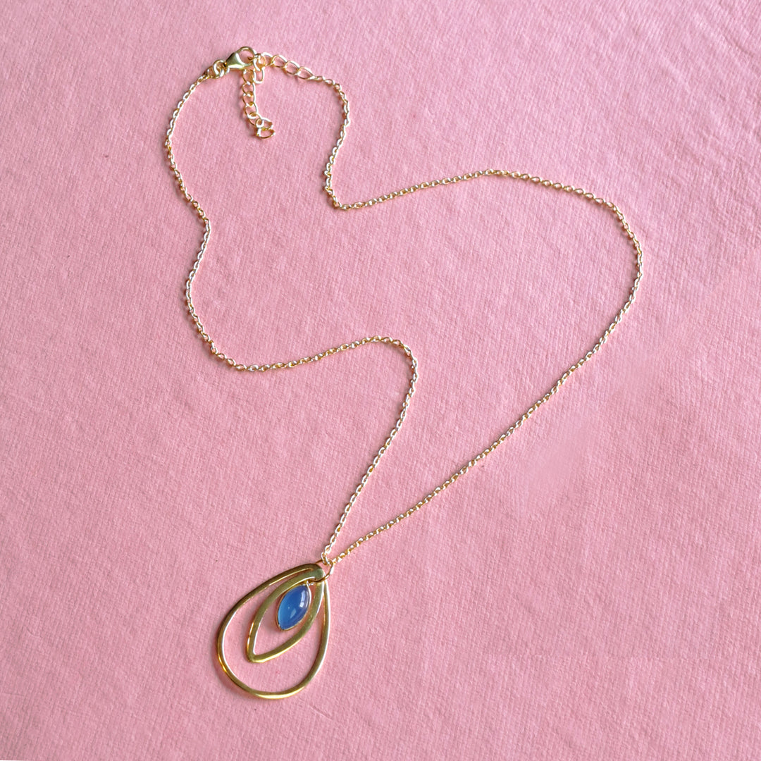 Gold teardrop pendant featuring a natural blue chalcedony cabochon on a pink background.