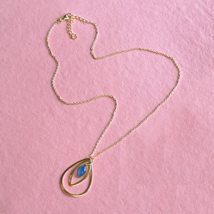 Gold teardrop pendant featuring a natural blue chalcedony cabochon on a pink background.