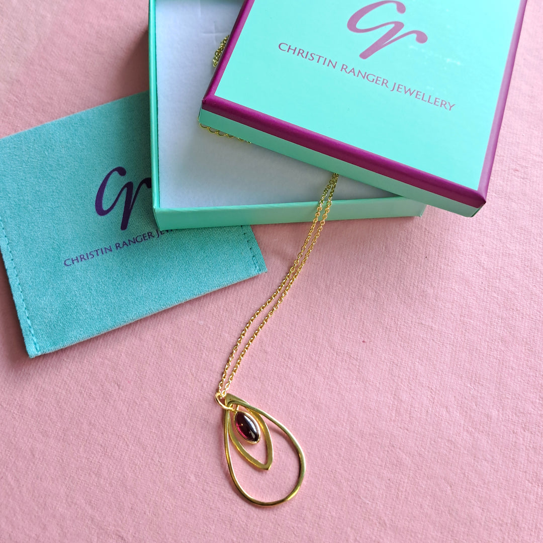 Gold Necklace with a red garnet cabochon gemstone in Christin Ranger Jewellery branded gift packaging.