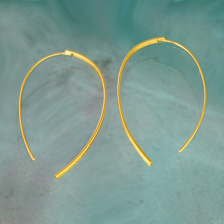 Gold threader hoop earrings on a textured green surface