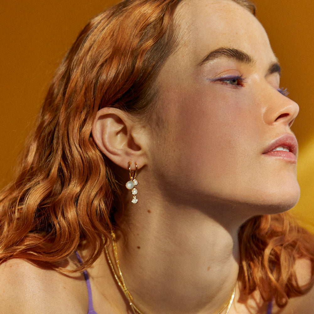 Model wearing two styles of gold moonstone earrings as a set.